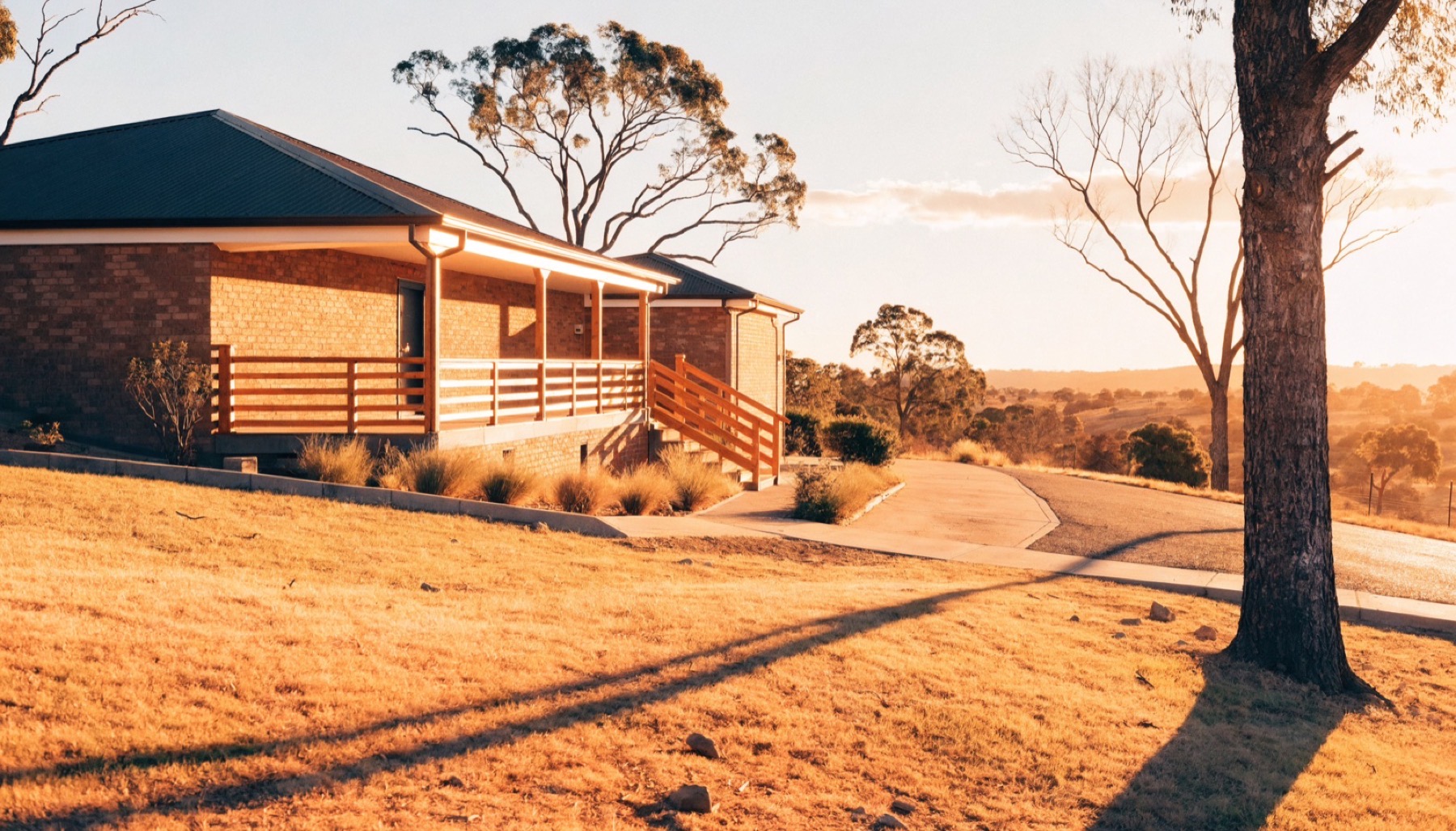 A brick home at golden hour with a concrete driveway curving past gum trees