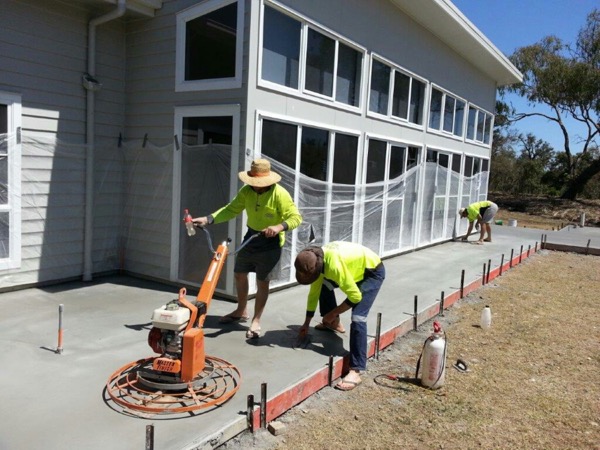 Two concreters power-trowelling a fresh slab beside a commercial building