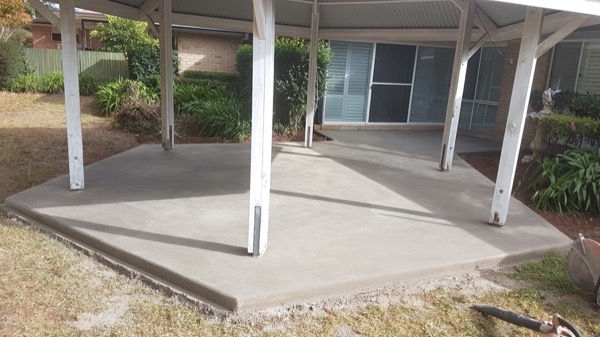A concrete slab under a carport at a brick home