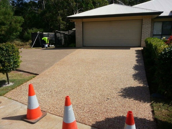 A tan exposed aggregate driveway leading to a double garage