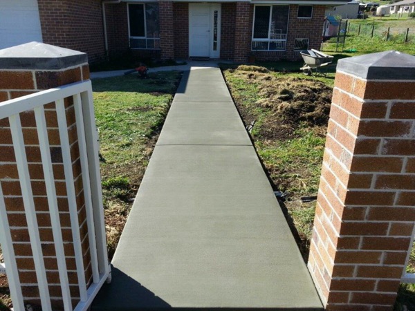 A concrete path running between two brick pillars toward a house