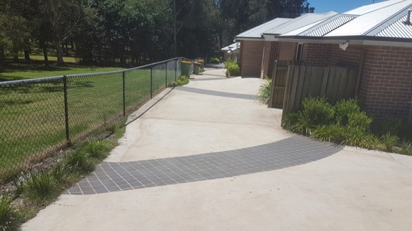 A concrete driveway with a dark charcoal border curving toward a carport