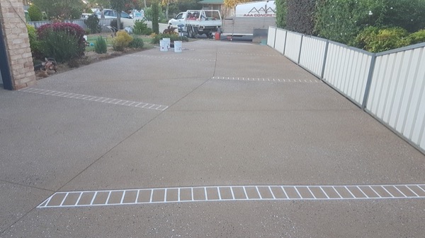 An exposed aggregate driveway with white stencil banding beside a shed