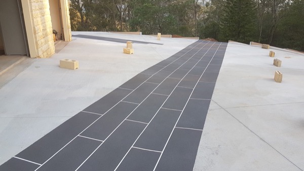 A concrete driveway with a dark stencilled path running to a garage