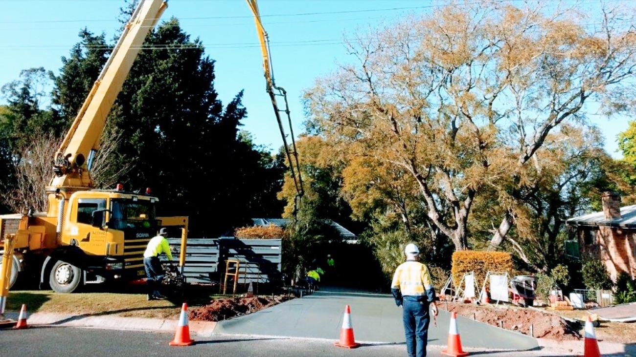 A concrete pump truck and crew placing a slab beside a suburban road