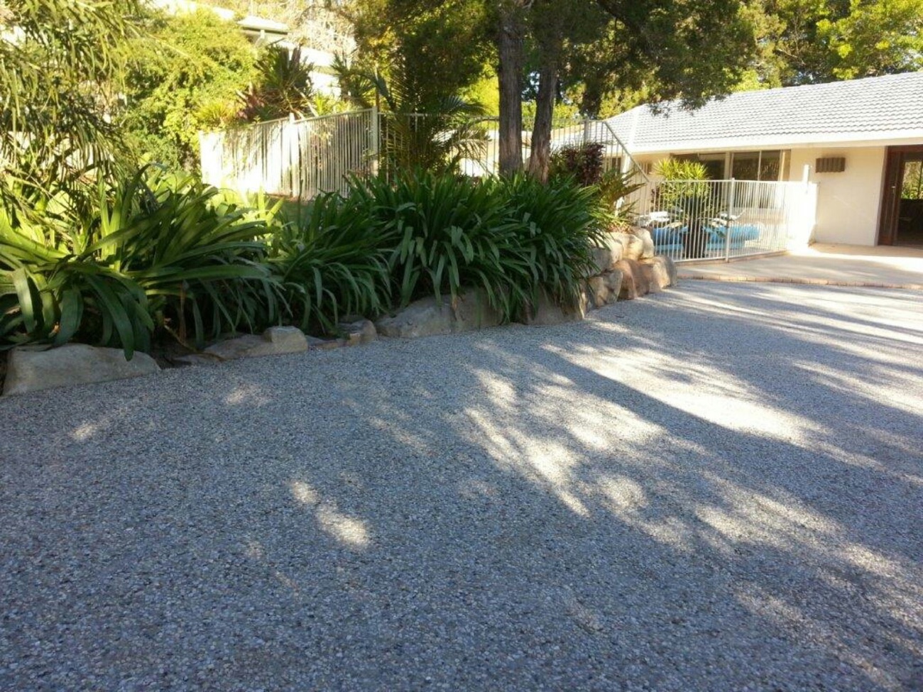 A washed exposed aggregate driveway running past a shaded garden bed