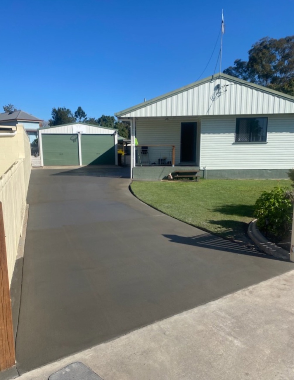 A plain grey concrete driveway running past a shed to a weatherboard house
