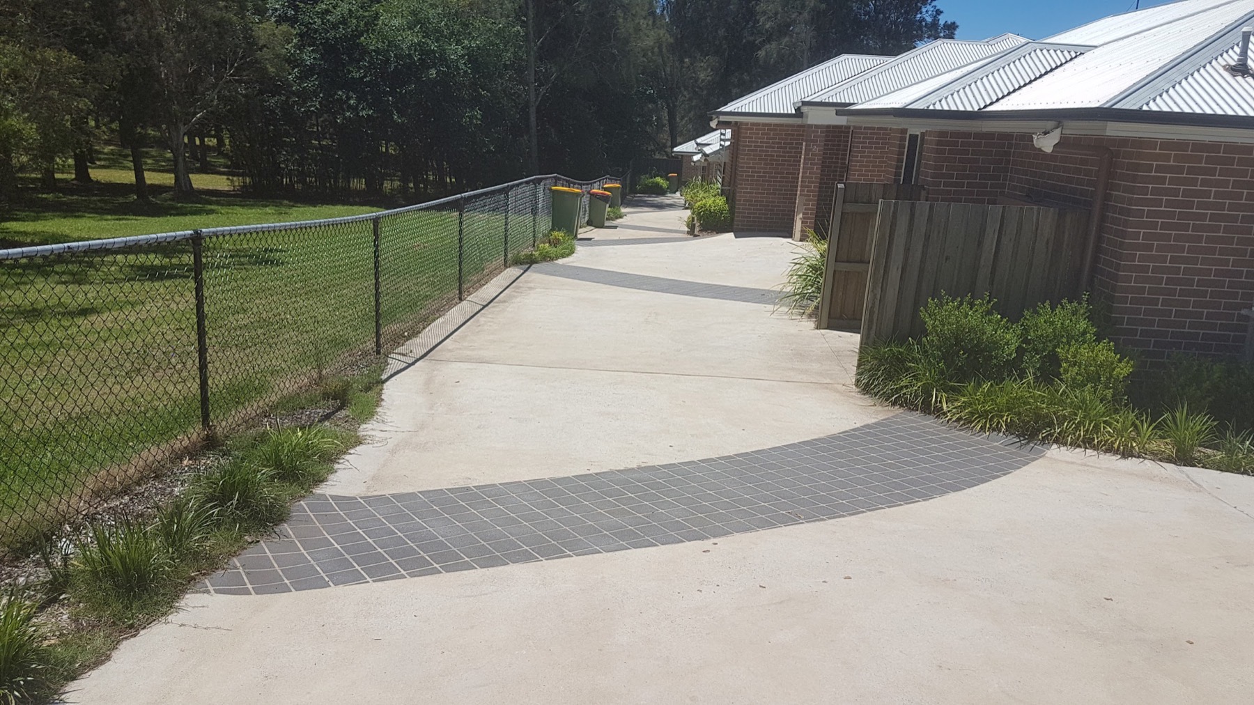 A concrete driveway with a dark charcoal border curving toward a carport