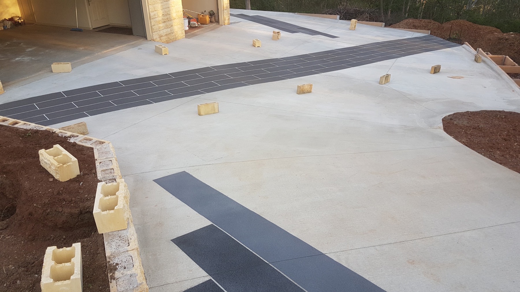 A concrete driveway with dark charcoal inlay bands beside a garage