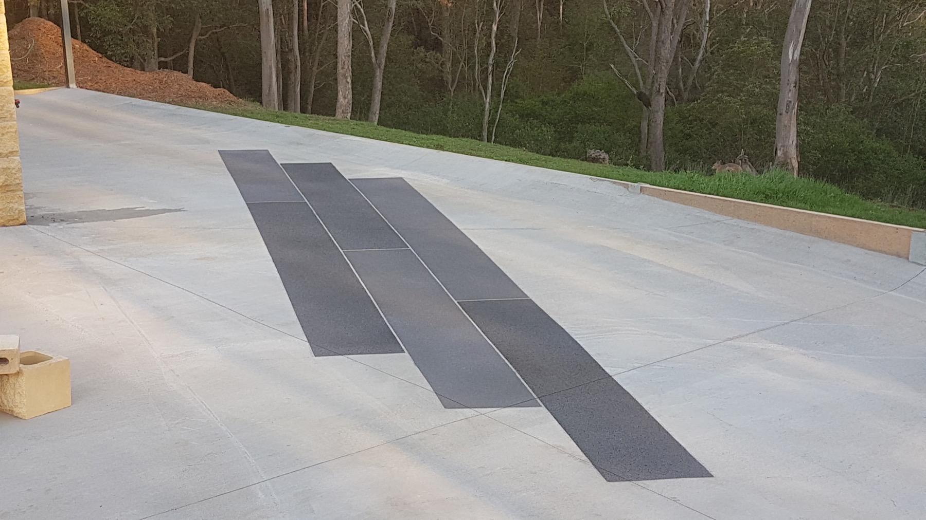 A wide concrete driveway with dark inlay strips running between gum trees