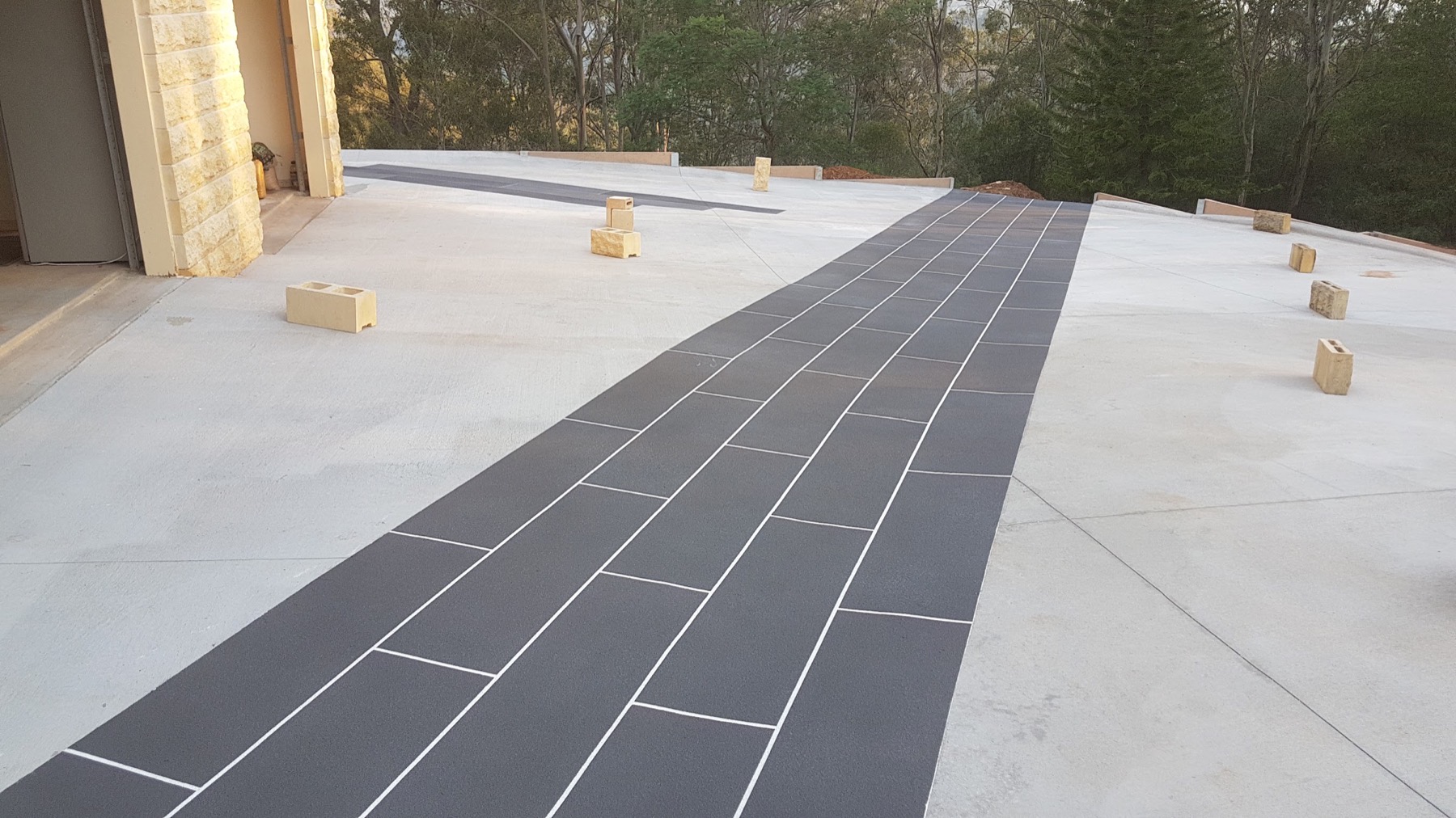 A concrete driveway with a dark stencilled path running to a garage